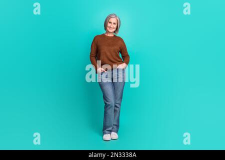 Ritratto di dimensioni complete di bella signora piuttosto anziana mettere le mani tasche in posa isolato su sfondo di colore turchese Foto Stock