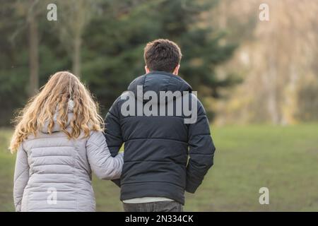Giovane coppia a piedi attraverso un parco di campagna lontano dalla fotocamera in primavera. Donna bionda e uomo dai capelli scuri. Foto Stock