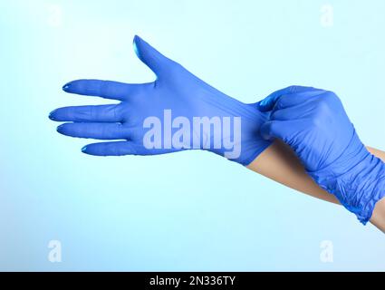 Donna che indossa guanti in lattice su sfondo azzurro, primo piano delle mani Foto Stock