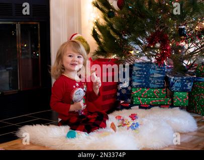 Una bella bionda bionda caucasica sotto l'albero di Natale la mattina di Natale. Regali di apertura per bambini Foto Stock