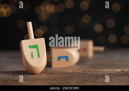 Hanukkah tradizionale dreidil con lettera lui su tavola di legno contro le luci sfocate, spazio per il testo Foto Stock