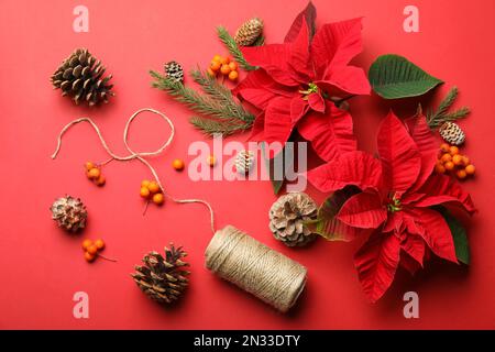 Composizione piatta con poinsettie (fiori di Natale tradizionali) e decorazioni su sfondo rosso Foto Stock