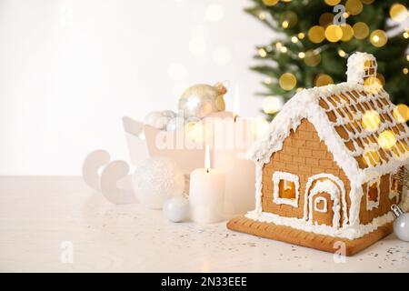 Bella casa di pan di zenzero decorata con glassa e candele su tavolo bianco Foto Stock