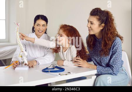 Madre felice e figlia piccola che guarda il modello anatomico della colonna vertebrale presso l'ufficio del medico Foto Stock