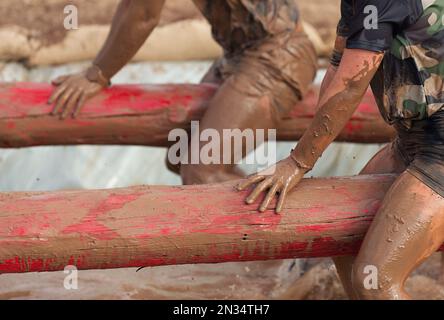 Corridori di corsa di fango. Partecipanti sul tronco dell'albero, cattura l'equilibrio sopra la fossa piena di acqua Foto Stock