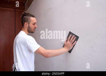 White Man ripara la parete bianca utilizzando carta vetrata Foto Stock