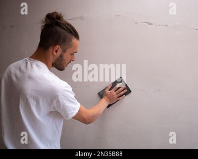 White Man ripara la parete bianca utilizzando carta vetrata Foto Stock