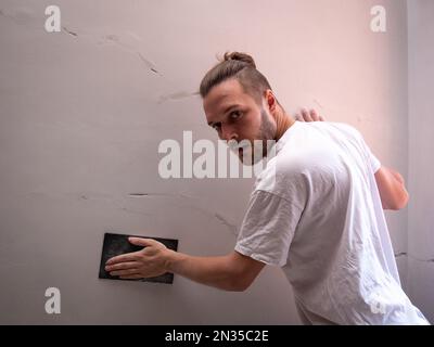 White Man ripara la parete bianca utilizzando carta vetrata Foto Stock