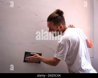 White Man ripara la parete bianca utilizzando carta vetrata Foto Stock