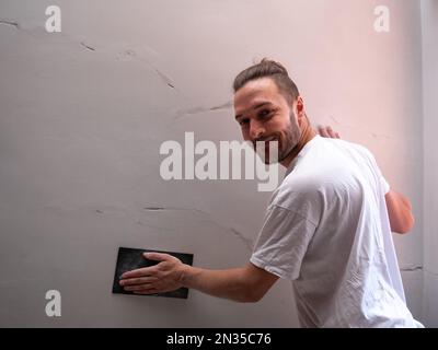 White Man ripara la parete bianca utilizzando carta vetrata Foto Stock