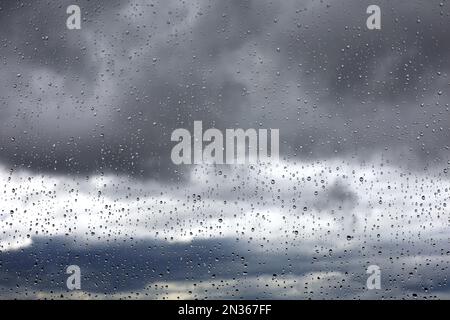 Gocce di pioggia sul vetro della finestra su sfondo sfocato del cielo con nuvole di tempesta. Bellissime gocce d'acqua, tempo durante la pioggia Foto Stock