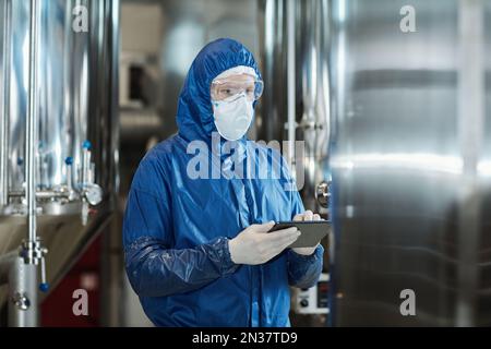 Rialzate il ritratto dell'operaio indossando l'equipaggiamento protettivo e la maschera usando il tablet in fabbrica industriale Foto Stock