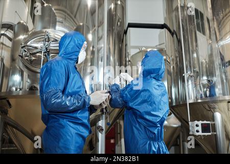 Vista posteriore di due lavoratori che indossano tute protettive durante il processo di produzione presso la fabbrica chimica Foto Stock