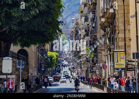 Le auto che guidano sulla strada con persone che camminano tra gli edifici di Palermo, Sicilia, Italia Foto Stock