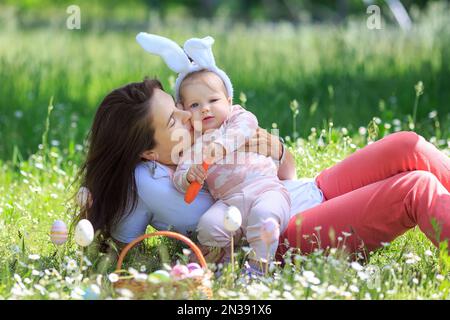 Famiglia felice al giorno di Pasqua che si diverte. Madre abbraccia, bacia ragazza divertente indossando orecchie di coniglio con carota. spazio di copia. Buona infanzia. Mamma, figlia celebrità Foto Stock