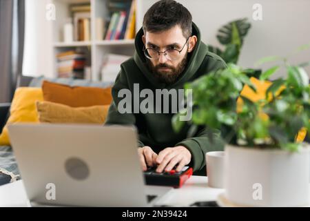 Uomo produttore di musica o arrangiatore utilizzando computer portatile e tastiera midi e altre apparecchiature audio per creare musica in casa studio. Battete facendo e organizzando Foto Stock