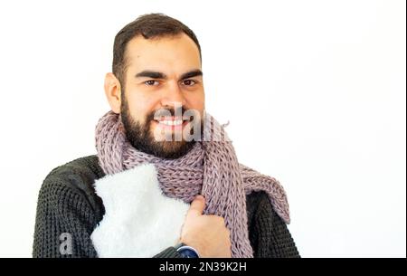 Giovane uomo portatore di abiti invernali in possesso di un sacchetto di acqua calda. Guardando la fotocamera. Sfondo bianco isolato. Foto Stock