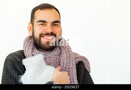 Giovane uomo portatore di abiti invernali in possesso di un sacchetto di acqua calda. Guardando la fotocamera. Sfondo bianco isolato. Foto Stock