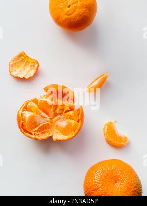 Vista dall'alto del tangerino pelato e intero. Buccia e pezzetti di agrumi su fondo bianco. Frutta fresca e brillante. Foto Stock