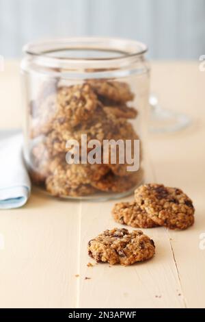 Biscotti di farina d'avena in un recipiente di vetro su una superficie di legno color crema Foto Stock