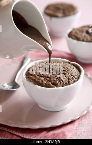Souffle di cioccolato individuale con salsa al cioccolato versato sulla parte superiore su sfondo rosa Foto Stock