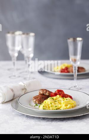 Brunch con uova strapazzate, polpettine di salsiccia, pomodori grigliati e bicchieri da champagne Foto Stock