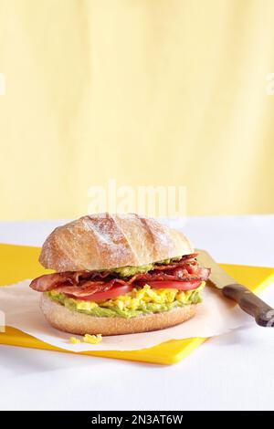 Panino per la colazione con pancetta, pomodoro, uova e purè di avocado su un panino Foto Stock