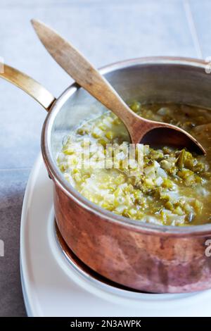 Salsa di tomatillo preparata in una pentola di rame con un cucchiaio di legno Foto Stock