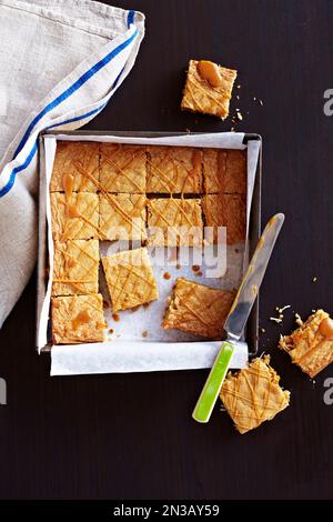 La blondie gocciolata al caramello viene quadrata in una padella con qualche ritaglio Foto Stock