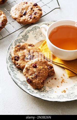 Biscotti per la colazione all'avena con mirtilli rossi su un piatto decorativo con una tazza di tè alle erbe Foto Stock