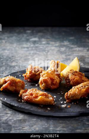 Ali di pollo impanate e salate con spicchi di limone su un piatto di ardesia Foto Stock