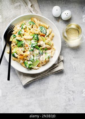 Rotini con broccoli in salsa di panna e un bicchiere di vino bianco su fondo grigio Foto Stock