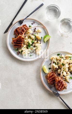 Due piatti di costolette di agnello alla griglia con insalata di cavolfiore su sfondo grigio Foto Stock