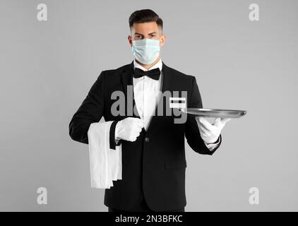 Cameriere in maschera medica con vassoio vuoto su sfondo grigio chiaro Foto Stock