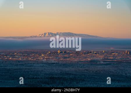 Il sole tramonta sul Monte Susitna, o Sleeping Lady, attraverso Cook Inlet dal centro di Anchorage, Alaska, sulla terra di Dena'ina, con la nebbia e il braccio Knik in vista Foto Stock