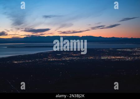 Il sole tramonta sopra il Monte Susitna, o Sleeping Lady, attraverso Cook Inlet dal centro di Anchorage, Alaska, sulla terra di Dena'ina, con il braccio di Knik in vista Foto Stock