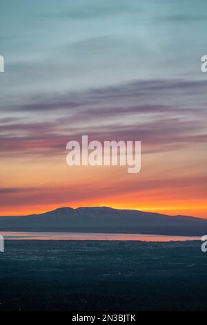 Il sole tramonta sopra il Monte Susitna, o Sleeping Lady, attraverso Cook Inlet dal centro di Anchorage, Alaska, sulla terra di Dena'ina, con il braccio di Knik in vista Foto Stock