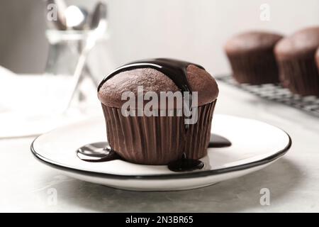 Delizioso cupcake fresco con sciroppo al cioccolato su tavolo in marmo grigio chiaro, primo piano Foto Stock