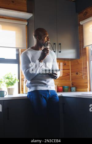 Uomo anziano afro-americano con occhiali e tavoletta che guarda lontano in cucina Foto Stock