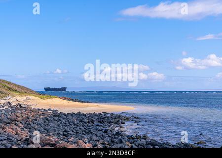 La costa rocciosa e sabbiosa di Shipwreck Beach a Lanai con un vecchio relitto navale arenato nella barriera corallina e l'isola di Maui in lontananza Foto Stock