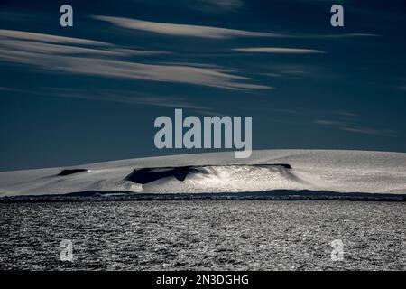 Il sole si riflette sul ghiaccio e sulla neve su un'isola di Anderson bagnata dal vento nello stretto antartico; Antartide Foto Stock