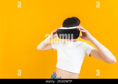 Donna che gioca con visore VR. Giochi per ragazze adulte con tecnologia di realtà virtuale. Studio interno girato su sfondo giallo. Foto di alta qualità Foto Stock