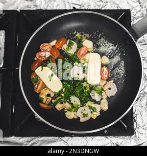 Vista dall'alto verso il basso dei tagliolini neri preparati in padella con gamberi al burro e salsa di pomodoro. Processo di preparazione del cibo della cucina del ristorante. Inquadratura quadrata per interni. Foto di alta qualità Foto Stock