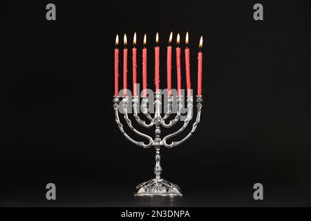 Menorah d'argento con candele accese su sfondo nero. Hanukkah celebrazione Foto Stock