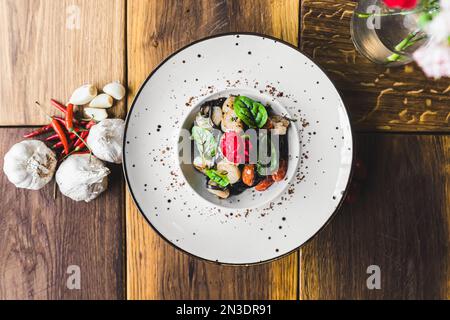 Vista dall'alto dei tagliolini neri con gamberi e pomodori secchi serviti su un piatto bianco su un tavolo di legno decorato con aglio e peperoni. Cucina italiana. Scatto orizzontale in interni. Foto di alta qualità Foto Stock