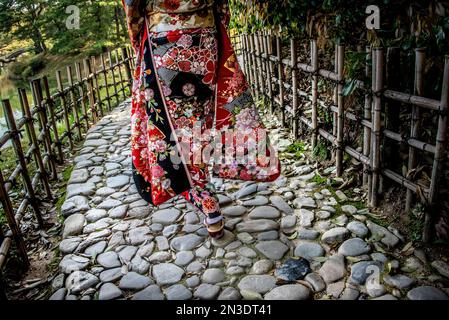 Donna con abbigliamento tradizionale giapponese che cammina nel Ritsurin Garden, un grande giardino storico a Takamatsu; Takamatsu, Shikoku, Giappone Foto Stock