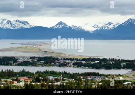 Un taxi galleggiante e decolla dal lago Beluga a Homer, Alaska, con una vista di Homer Spit, Kenai Mountains, e della città di Homer da una virginia... Foto Stock