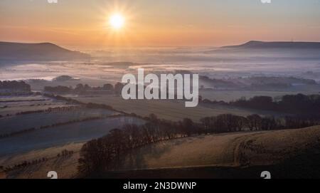 L'alba proietta lunghe ombre su un'inversione di nebbia mattutina che si estende sulla campagna inglese nel South Downs National Park Foto Stock