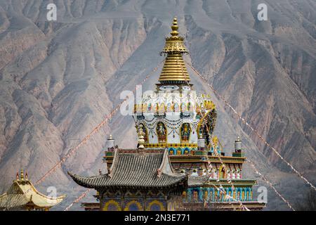 Il tetto di un tempio buddista presso il monastero di Labrang con le creste di montagna dell'Himalaya sullo sfondo; Labrang, Amdo, Tibet Foto Stock