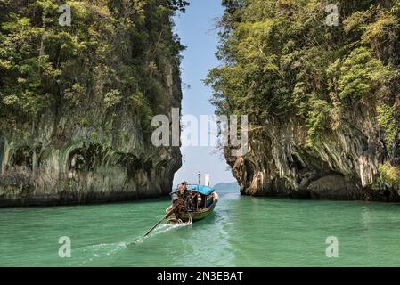 Tradizionale barca tailandese a coda lunga che viaggia attraverso le acque verdi e turchesi tra le vaste formazioni rocciose carsiche Foto Stock